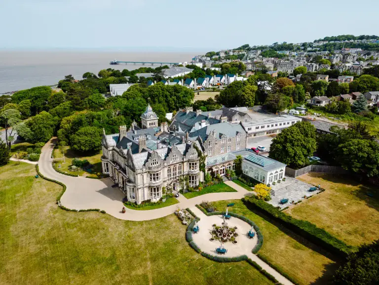 a large mansion with a large lawn and a large building with a body of water in the background