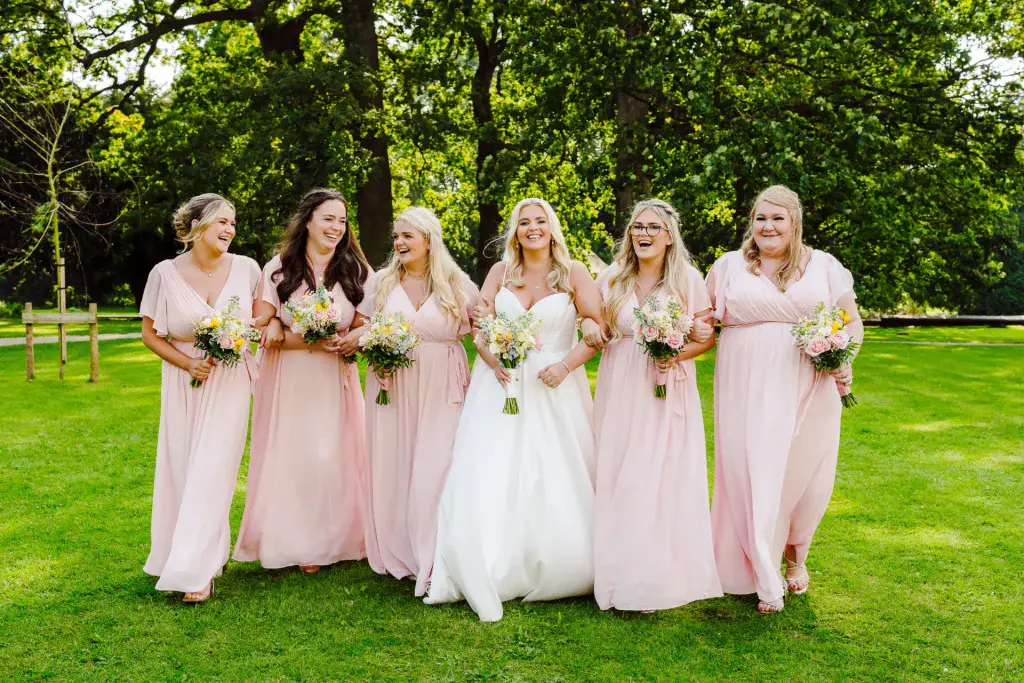 pink bridesmaid dresses on display as the bridal party walk towards the videographer and photographer smiling and laughing