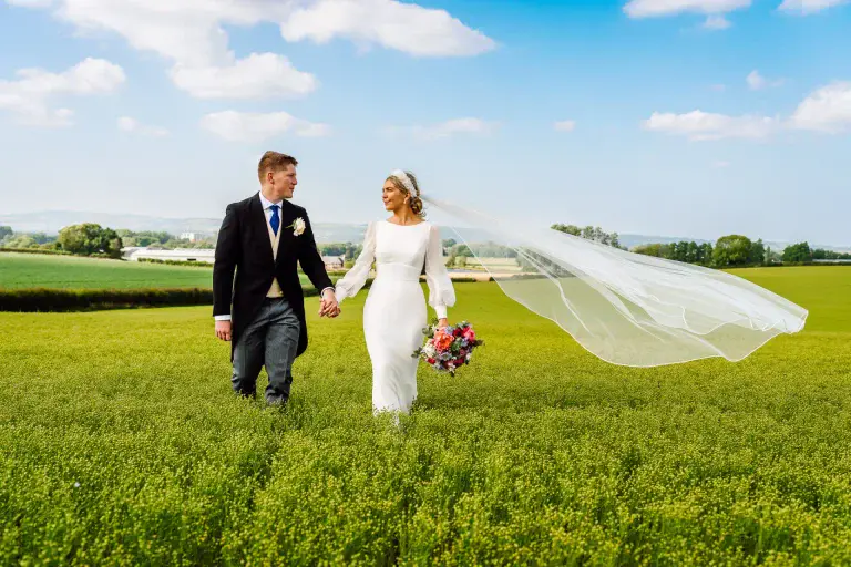 a man and woman holding hands and walking in a field in somerset