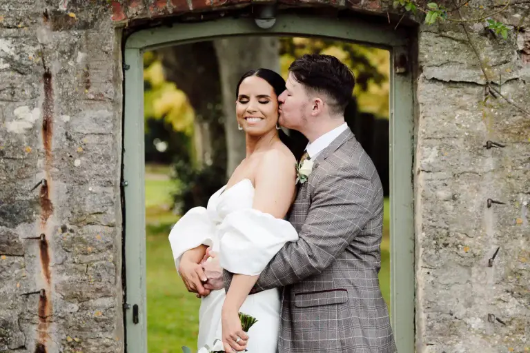 a man kissing a woman in a white dress in the gardens of coombe lodge wedding venue as captured by this somerset wedding videographer