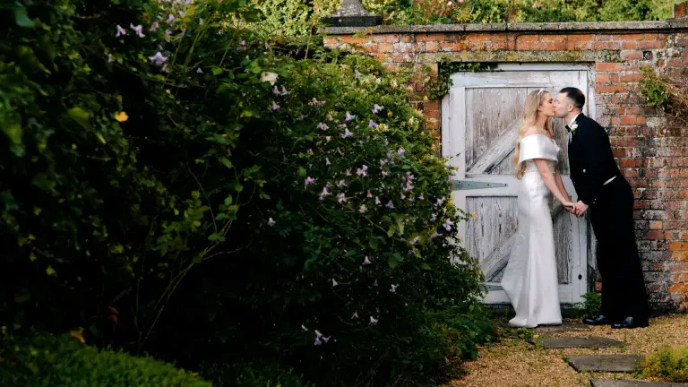 bride and groom kiss in secret garden doorway at syrencot in wiltshire