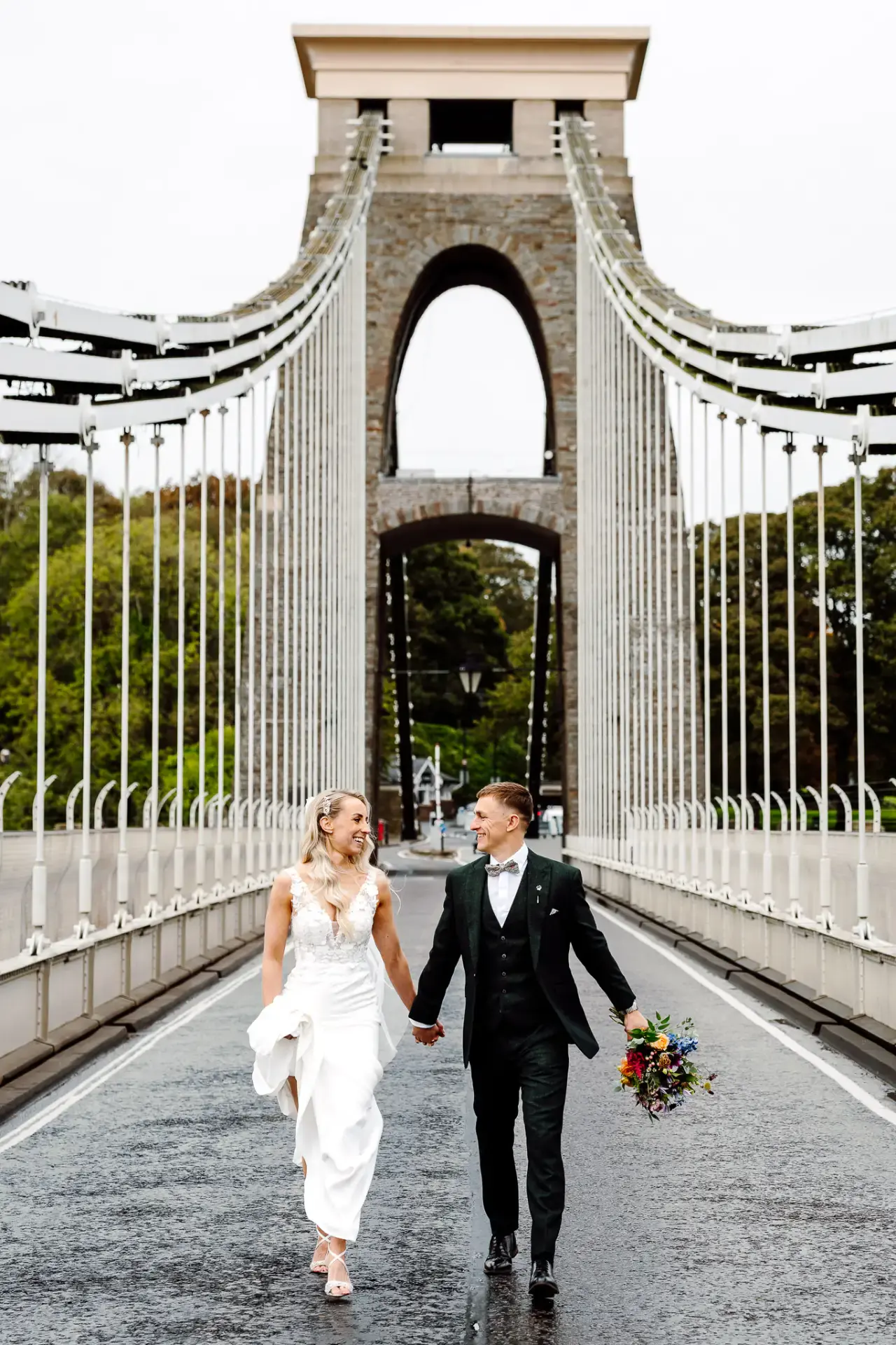 bride and groom walk down the middle of the clifton suspension bridge looking at one another in this example of bristol wedding videography