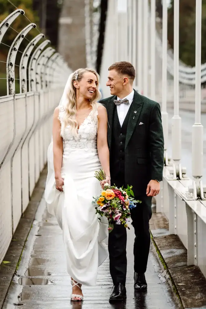 bride and groom walk down the middle of the clifton suspension bridge looking at one another in this example of bristol wedding videography