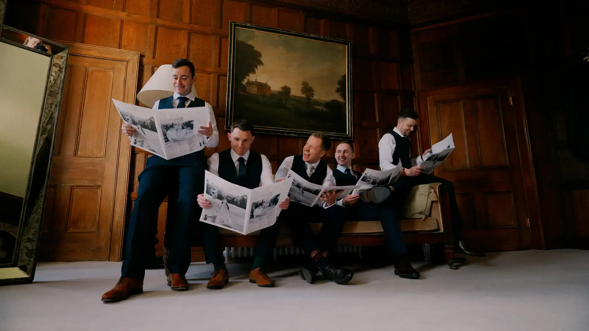 cotswolds wedding videographer captures the groomsmen reading the wedding day newspapers on the couch