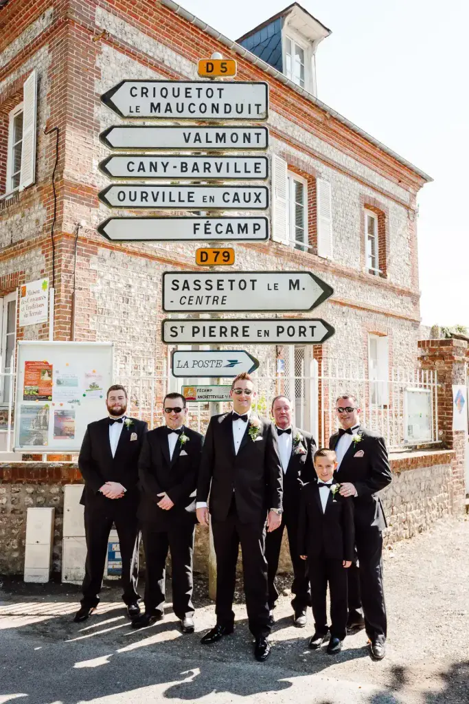 a group of groomsmen in black suits standing in front of a street sign in France on their wedding day